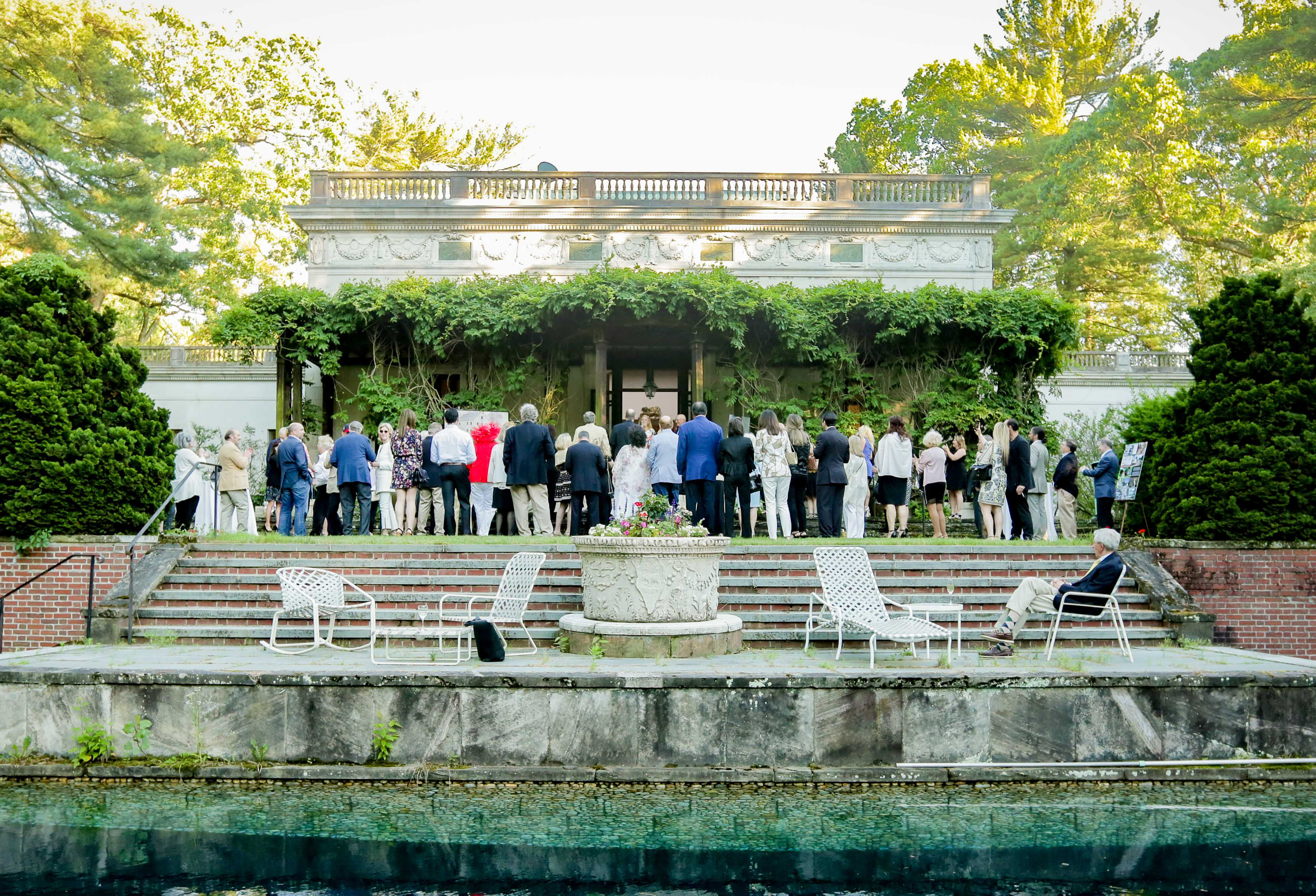 a group of people stand with their backs to the camera, in front of a stone building entrance framed by vines